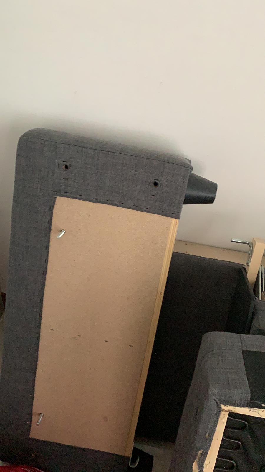 Partially assembled grey fabric sofa base showing exposed particle board and wooden frame structure.
