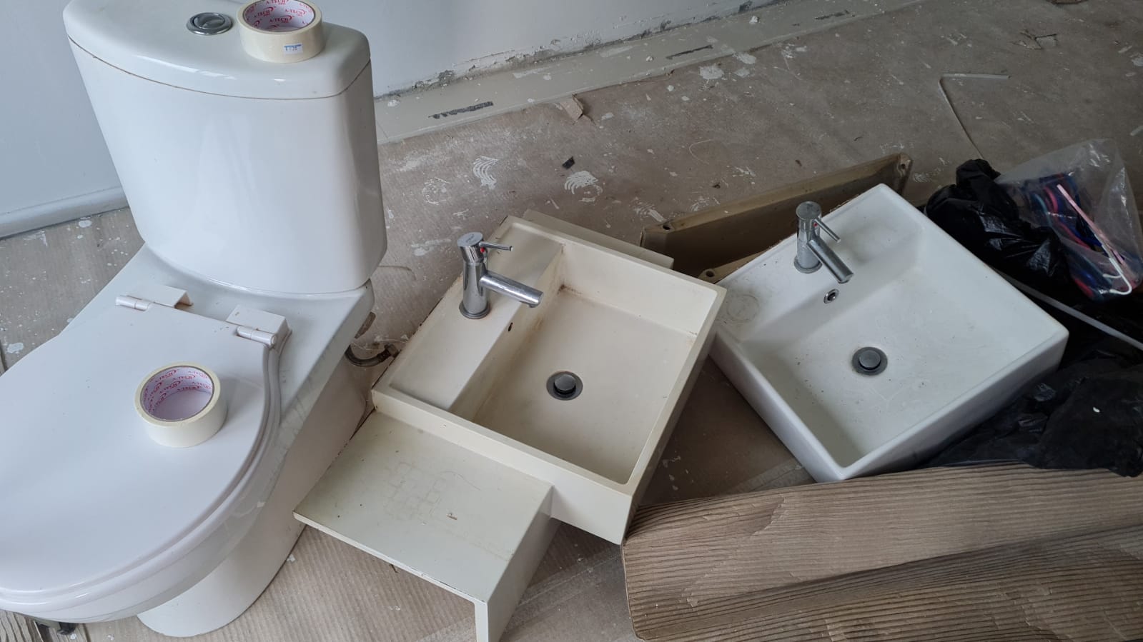 New toilet bowls and bathroom sink fixtures arranged on a construction site floor awaiting installation or removal.