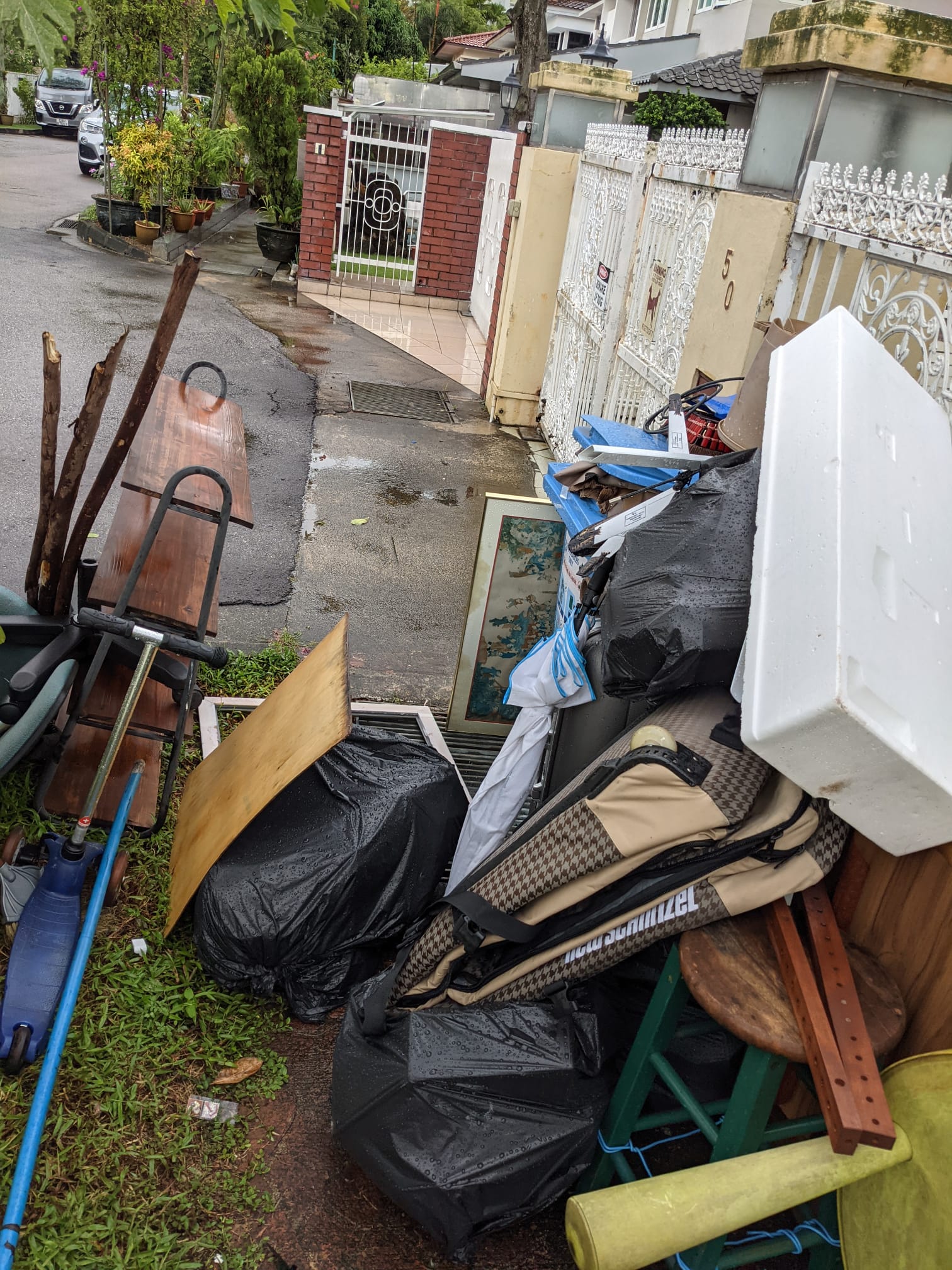 Wooden board, black refuse bags, and a patterned bag stacked together on a roadside.