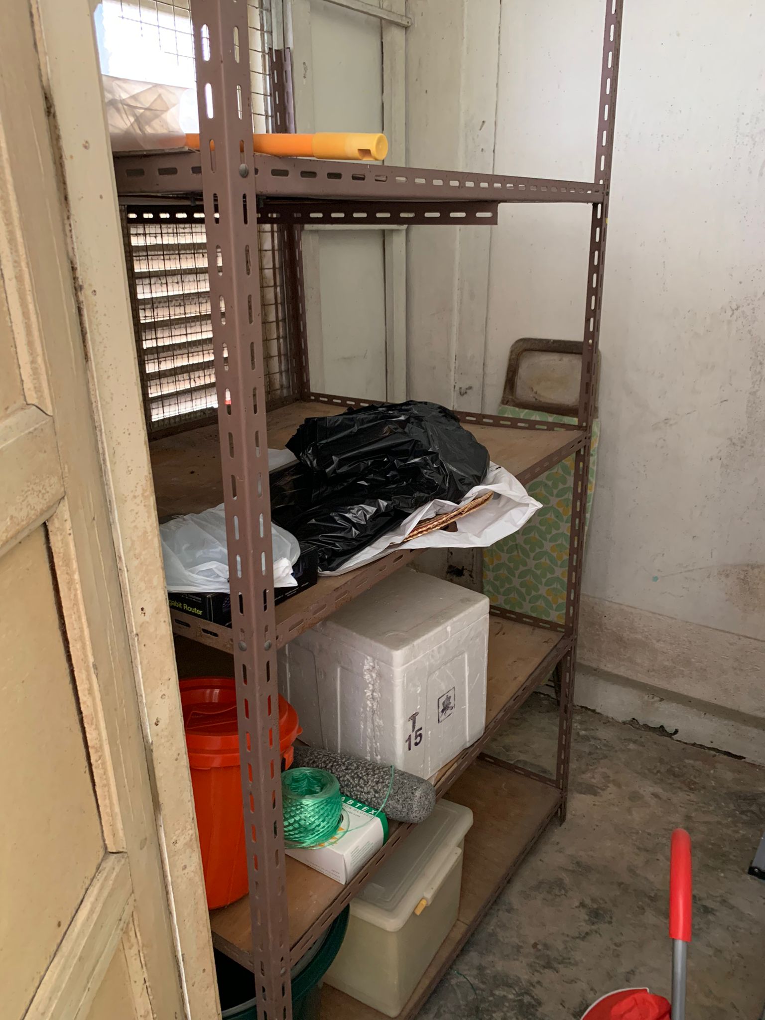 Shelving unit holding black trash bags, a styrofoam box, and plastic storage containers in a residential space.