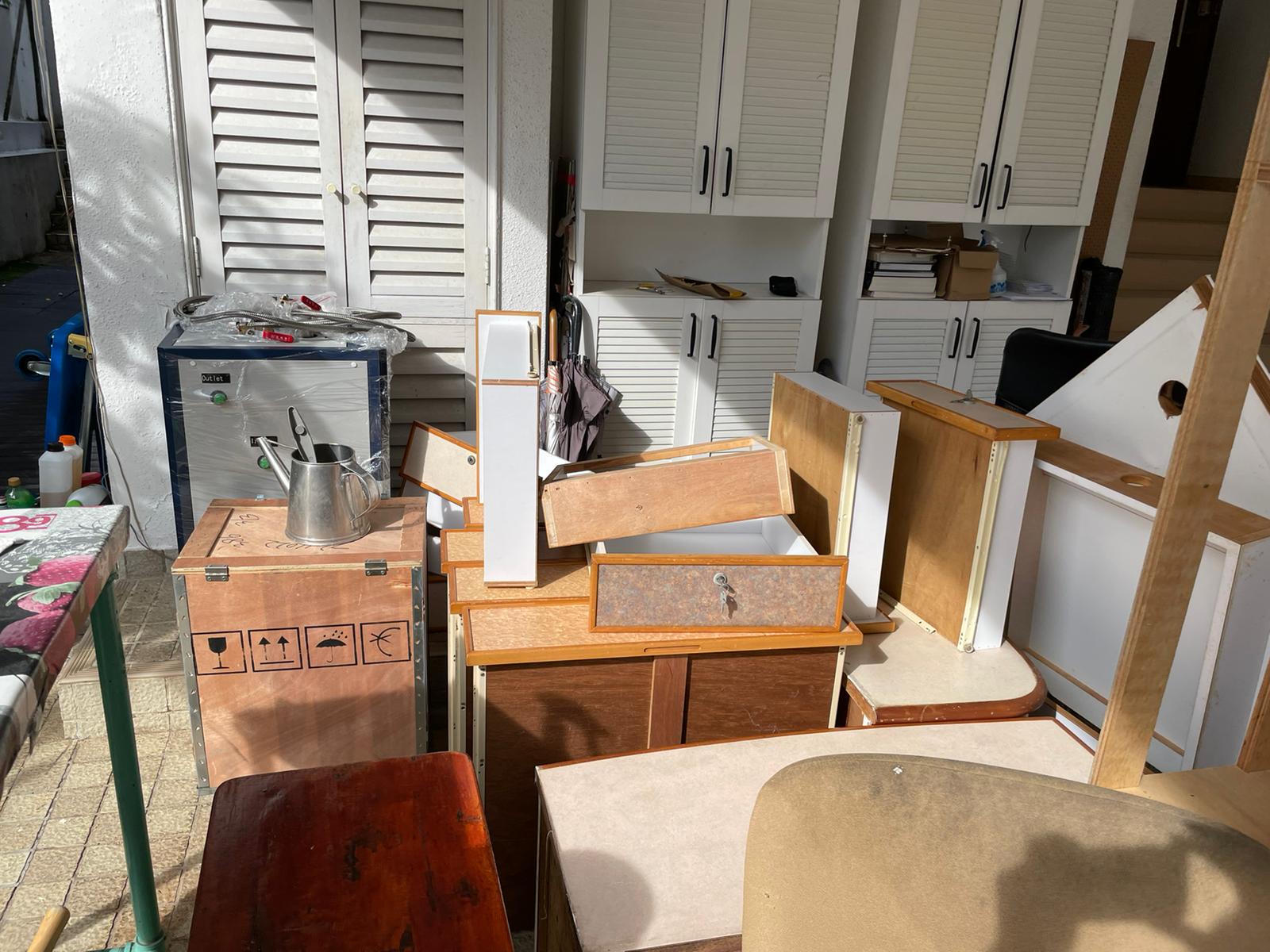 Pile of discarded wooden drawers, metal storage cabinet, and household items stacked outdoors in a residential area.
