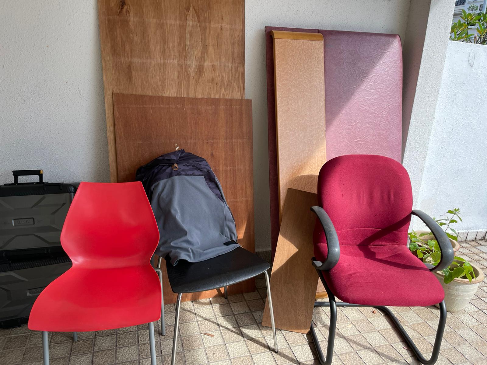 Red and maroon chairs, wooden boards, and a mattress stacked against a white wall in a residential space.