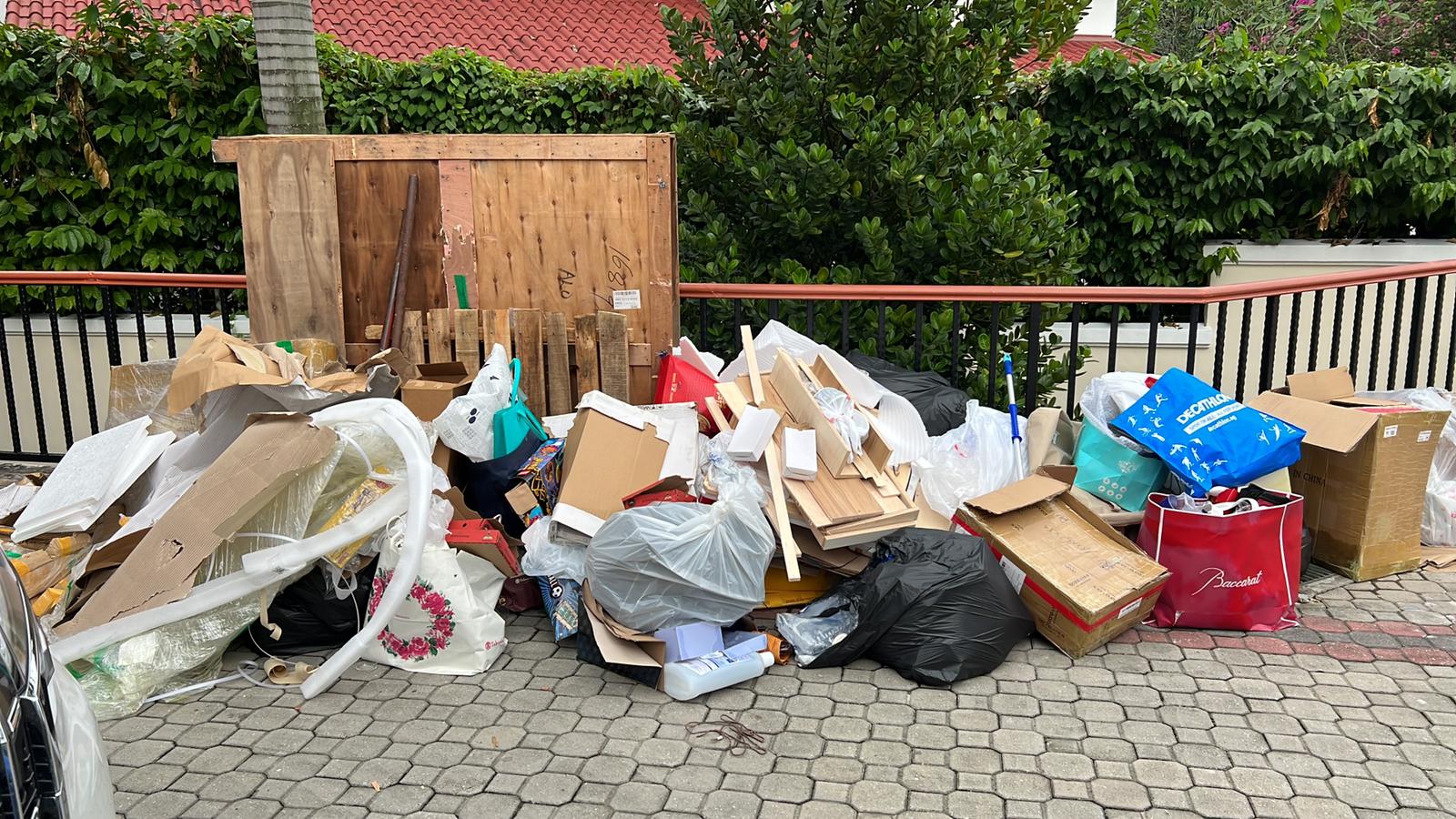 Accumulated household junk and flattened cardboard boxes stacked against a residential building fence.