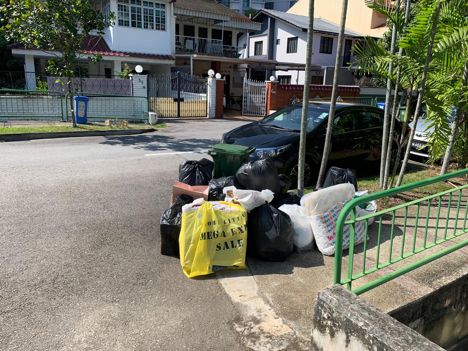 Black trash bags and a yellow promotional bag stacked on a residential street curb.