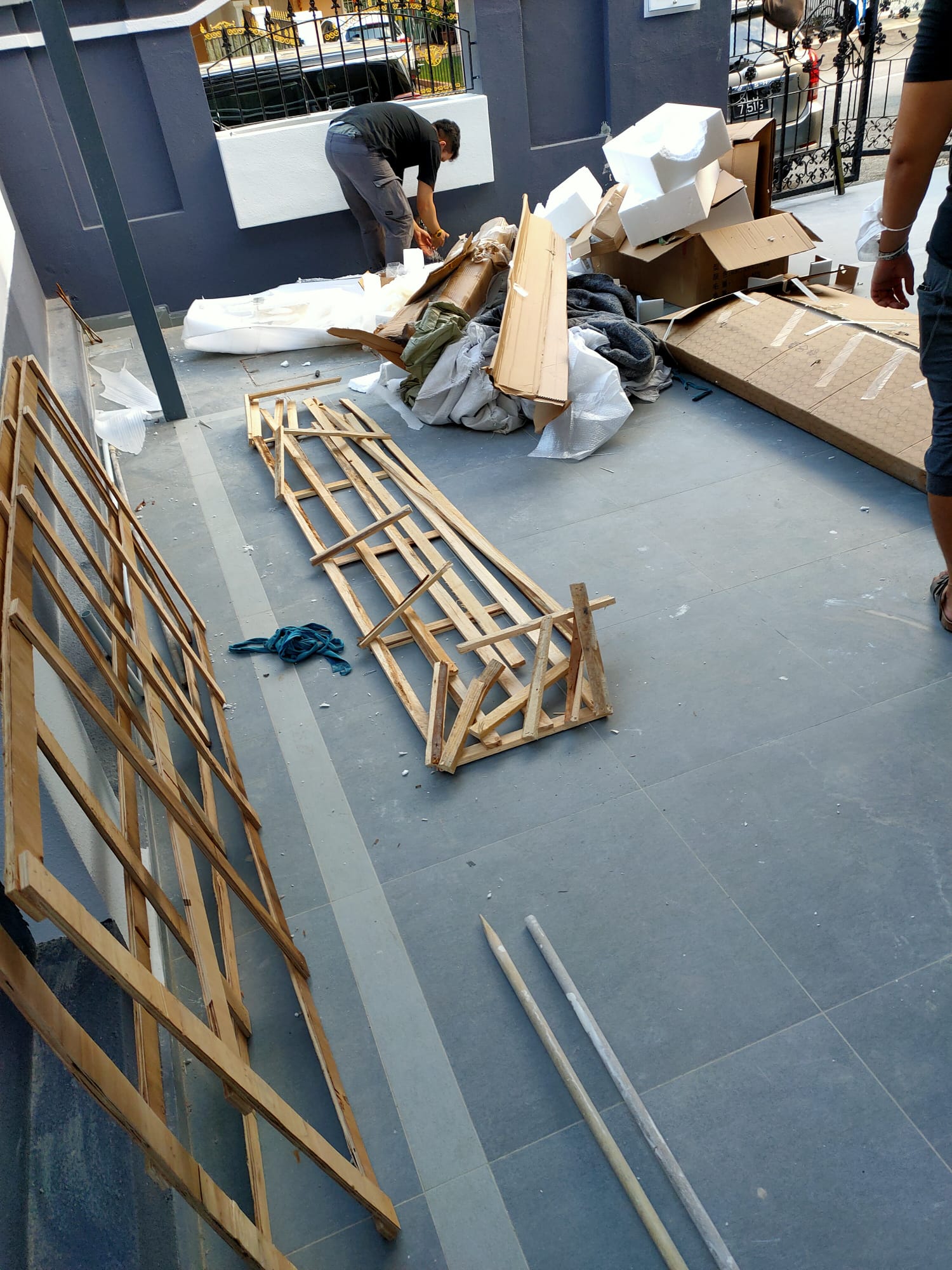 Wooden frames, packing materials, and mixed debris scattered on a tiled floor outside a residential building.