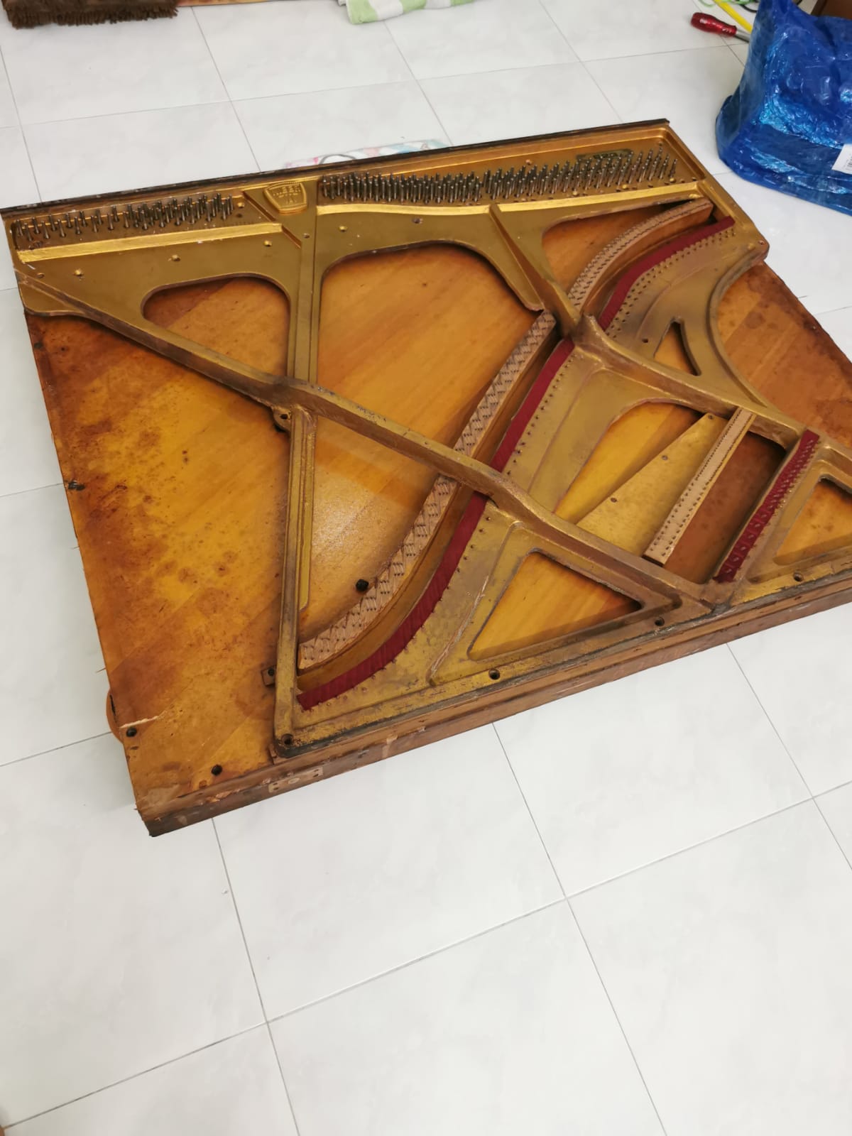 Disassembled piano soundboard and wooden frame laid out on a tiled residential floor, separated into components for removal.