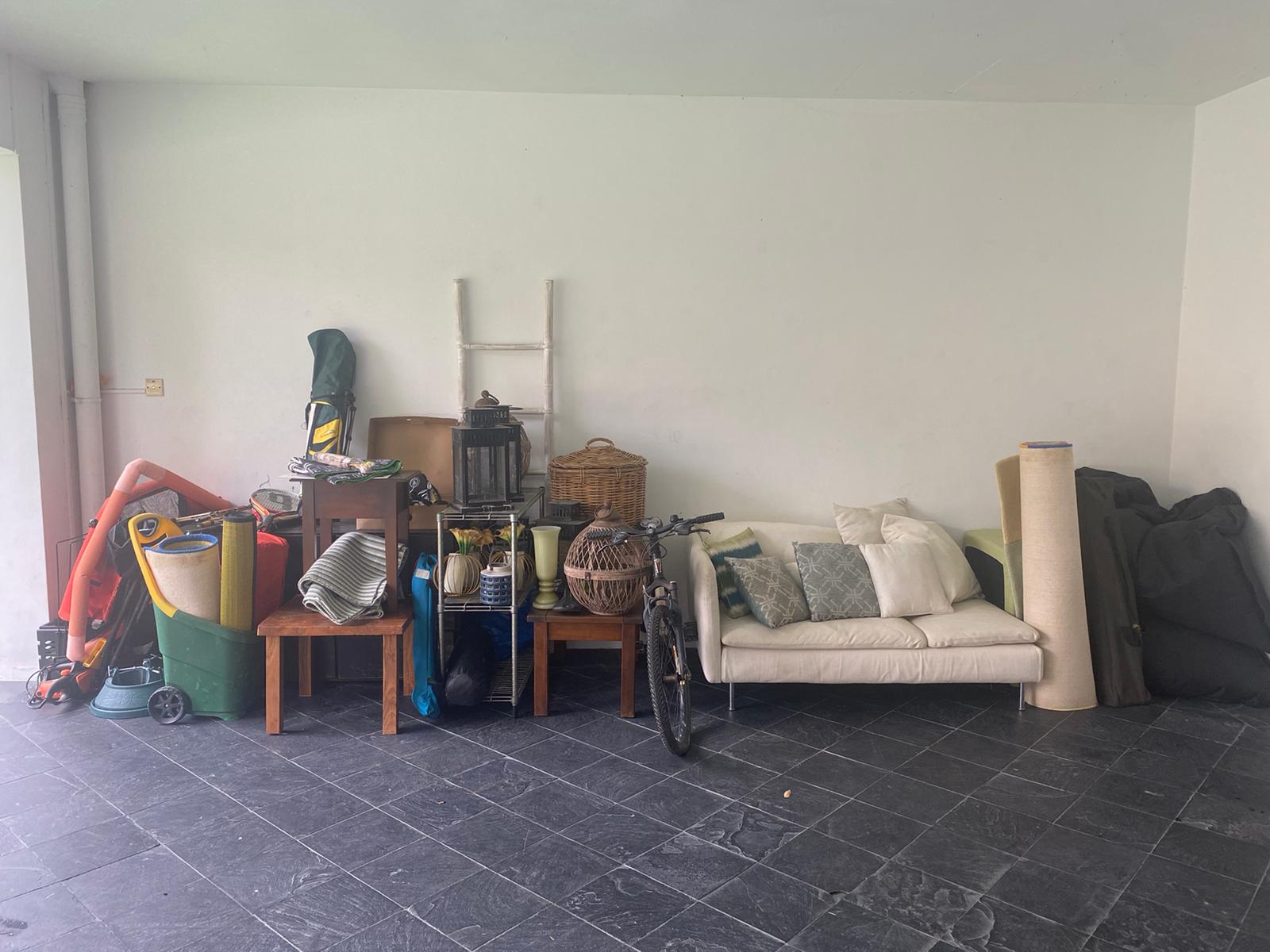 A cluttered residential room with a sofa, bicycle, and storage bins stacked against white walls and dark floor tiles.