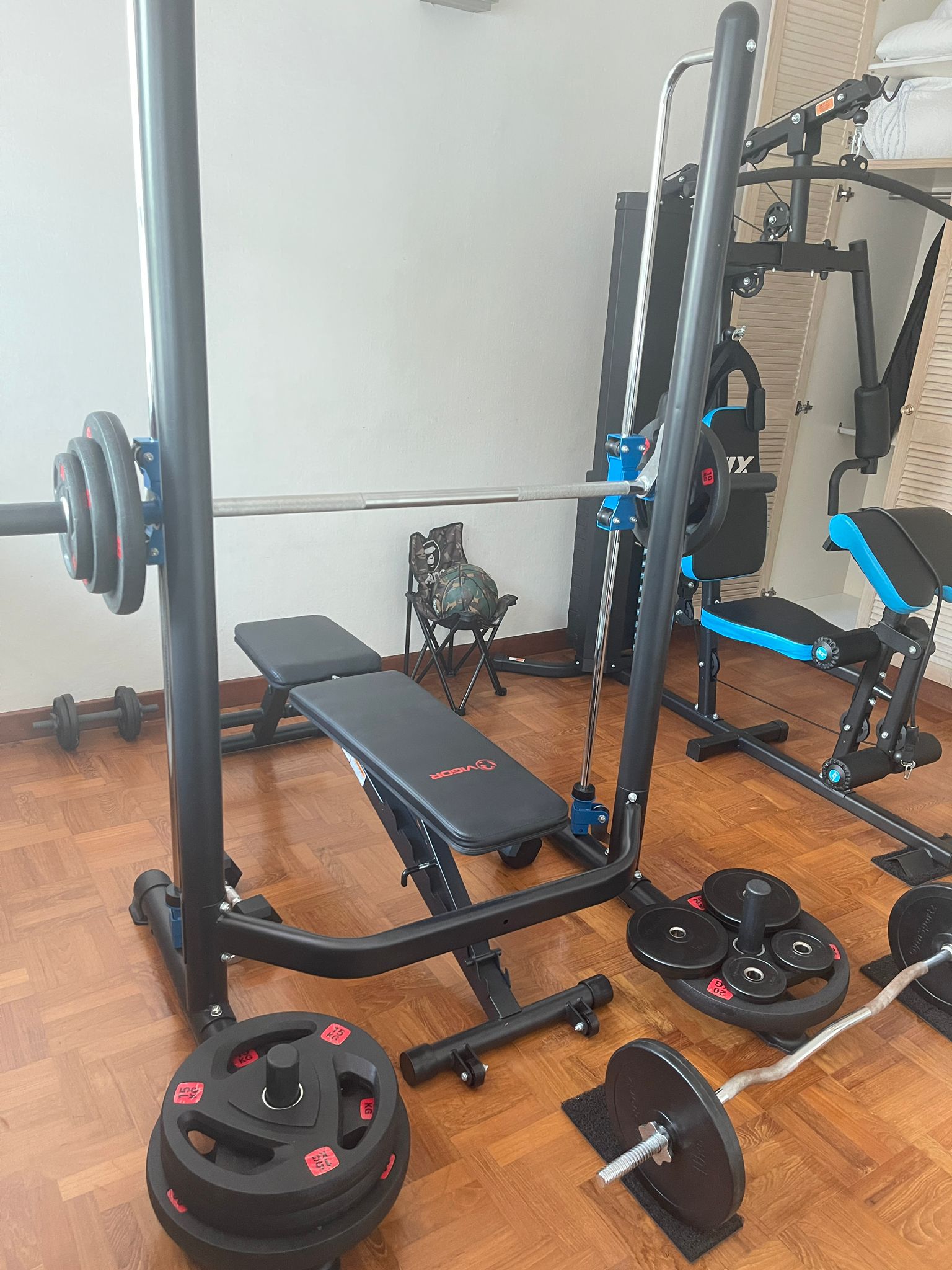 Home gym setup with weight bench, barbell, and stacked weight plates in a residential space.