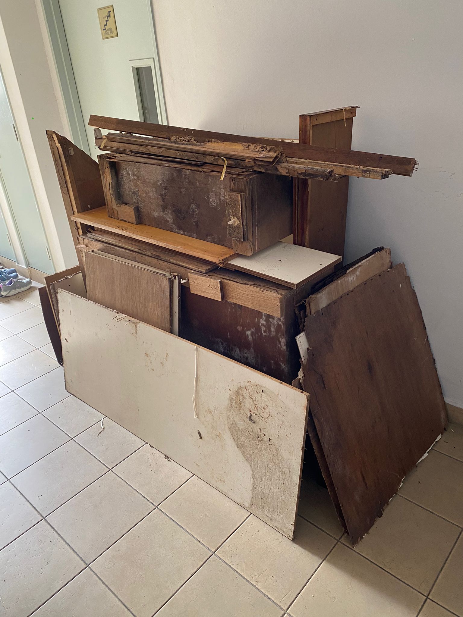 Stack of old wooden furniture and panels piled on a tiled residential floor.