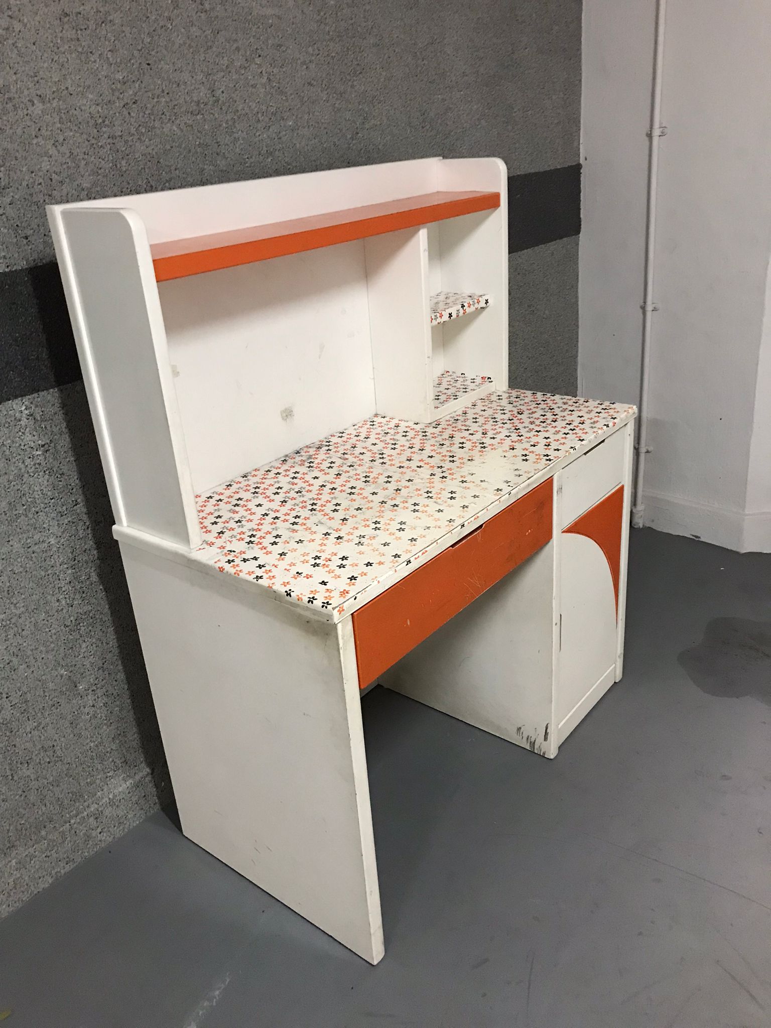 Vintage white and orange desk with patterned top surface, ready for disposal.