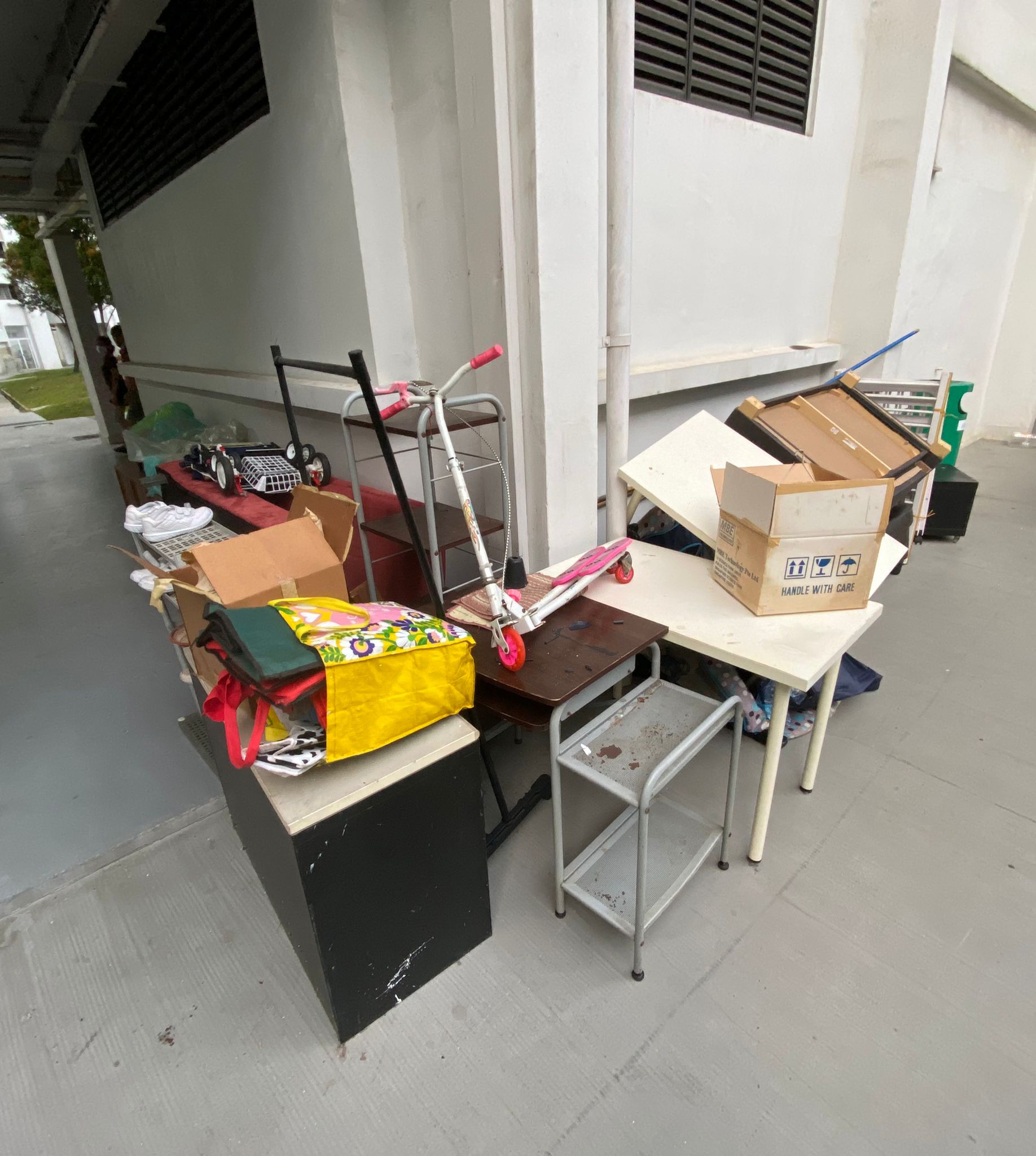 Scooter, cardboard boxes, and bags stacked on a HDB walkway outside a residential unit.