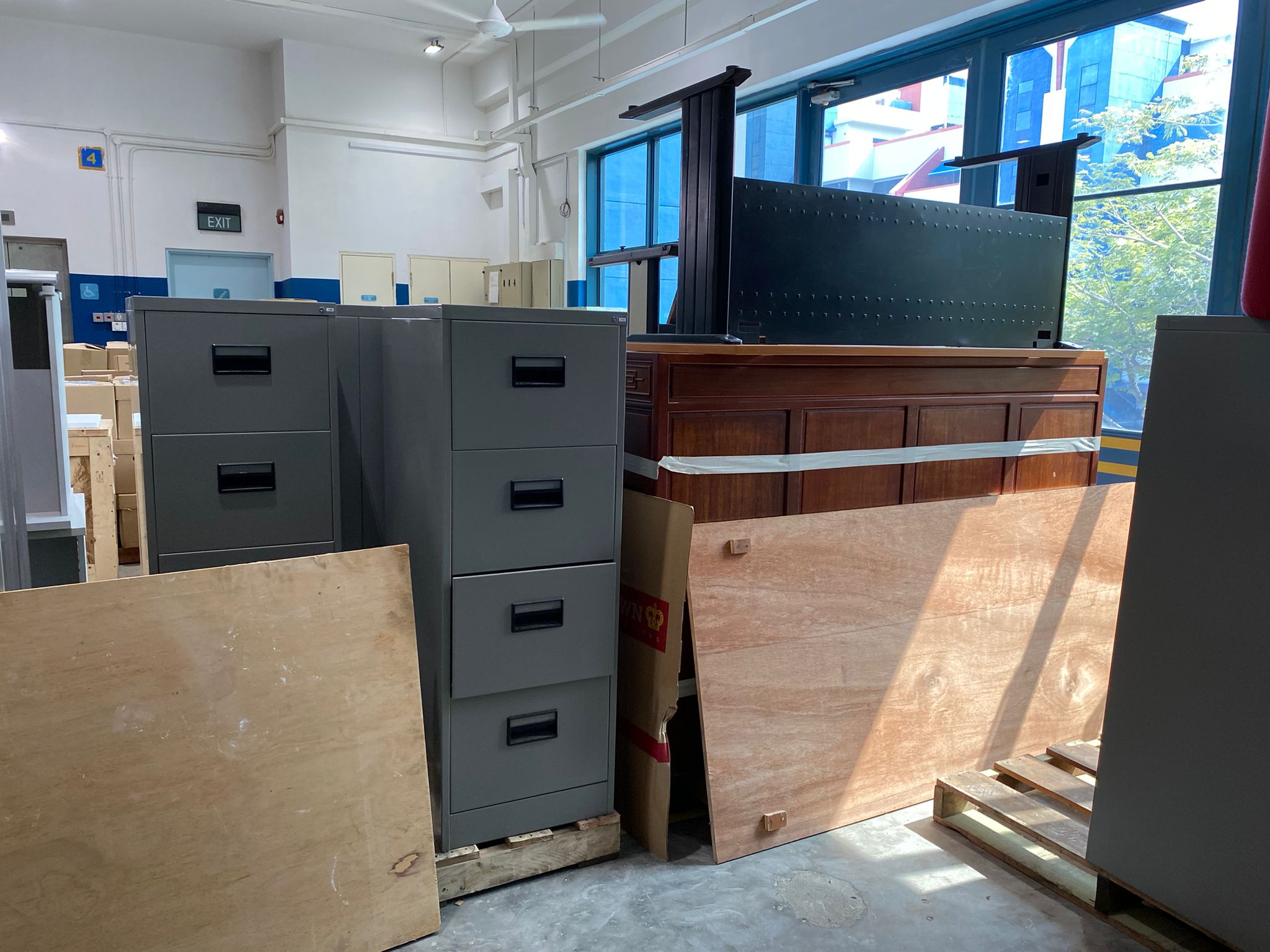 Stacked office filing cabinets and wooden furniture pieces ready for removal from an indoor commercial space.