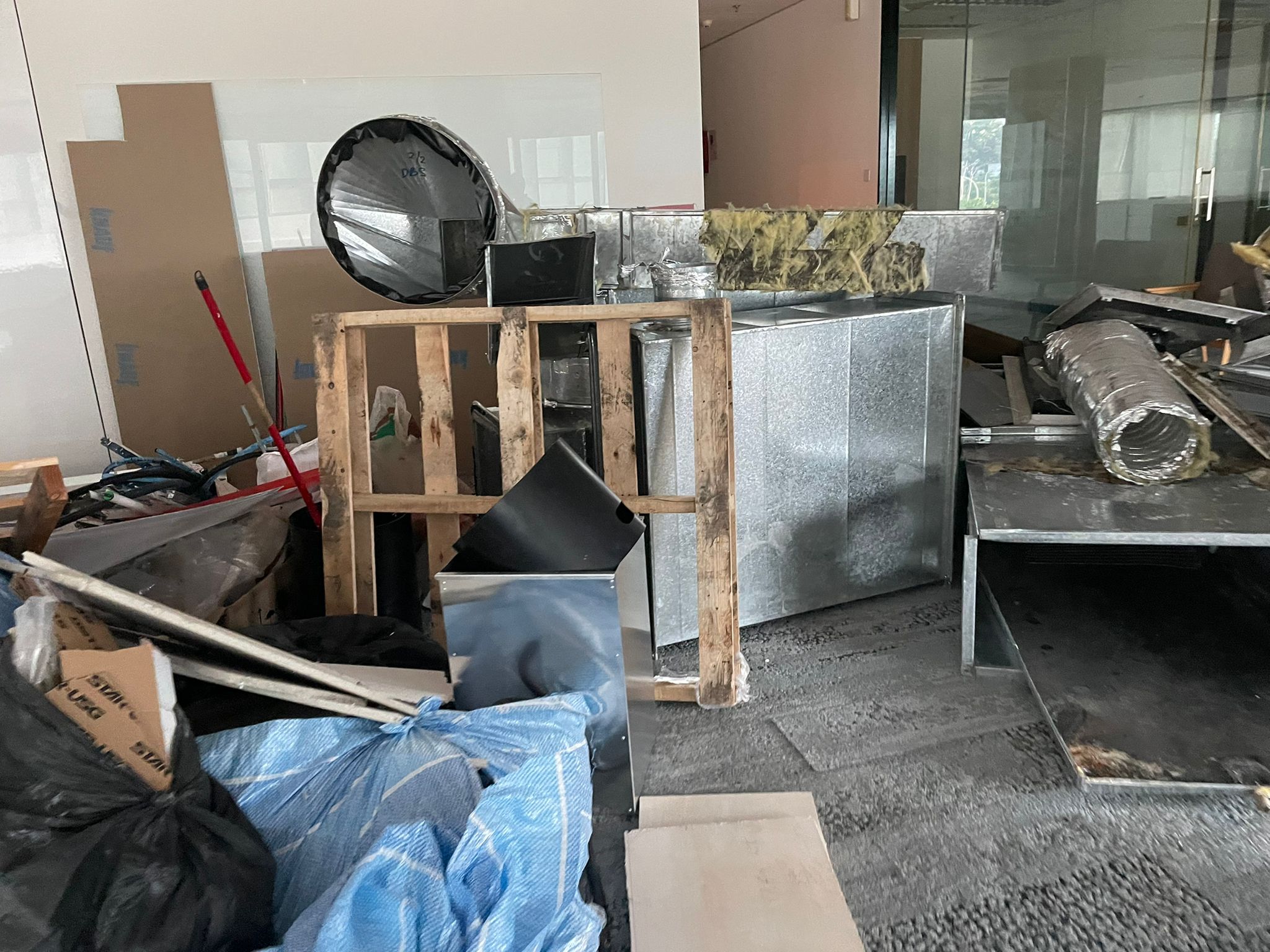 Office space with large metal ventilation ducts, wooden pallets, and mixed waste materials ready for removal.