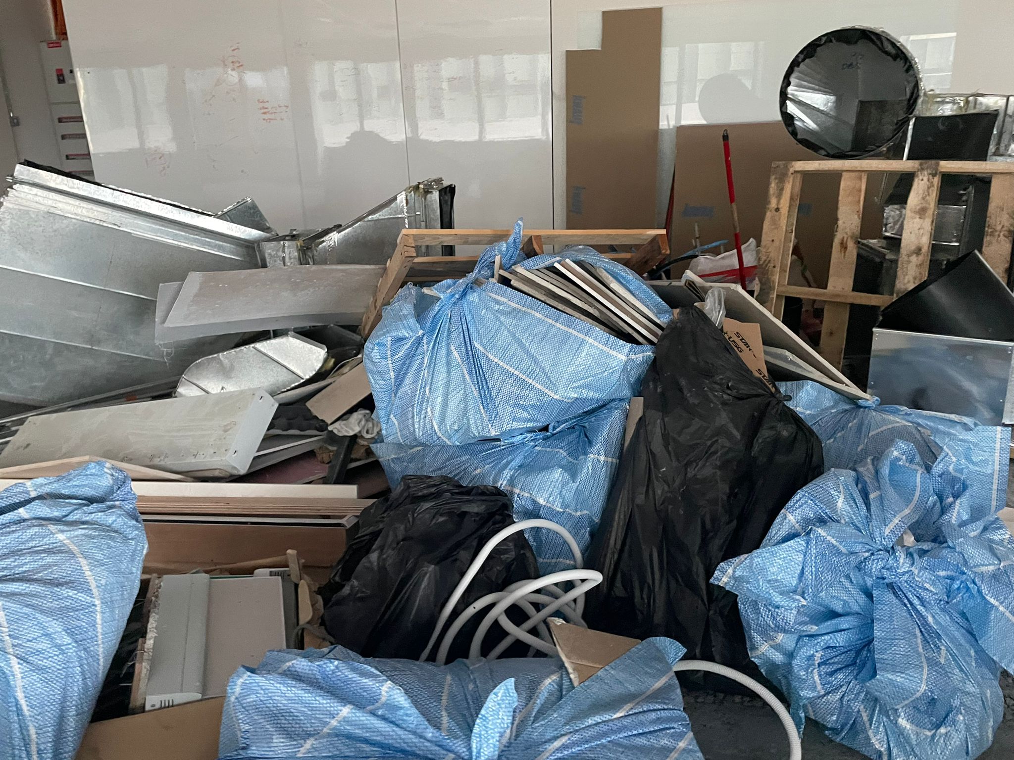 Commercial fit-out debris piled mid-renovation — bagged drywall offcuts, ductwork sheets, and stripped metal panels waiting for same-day removal.