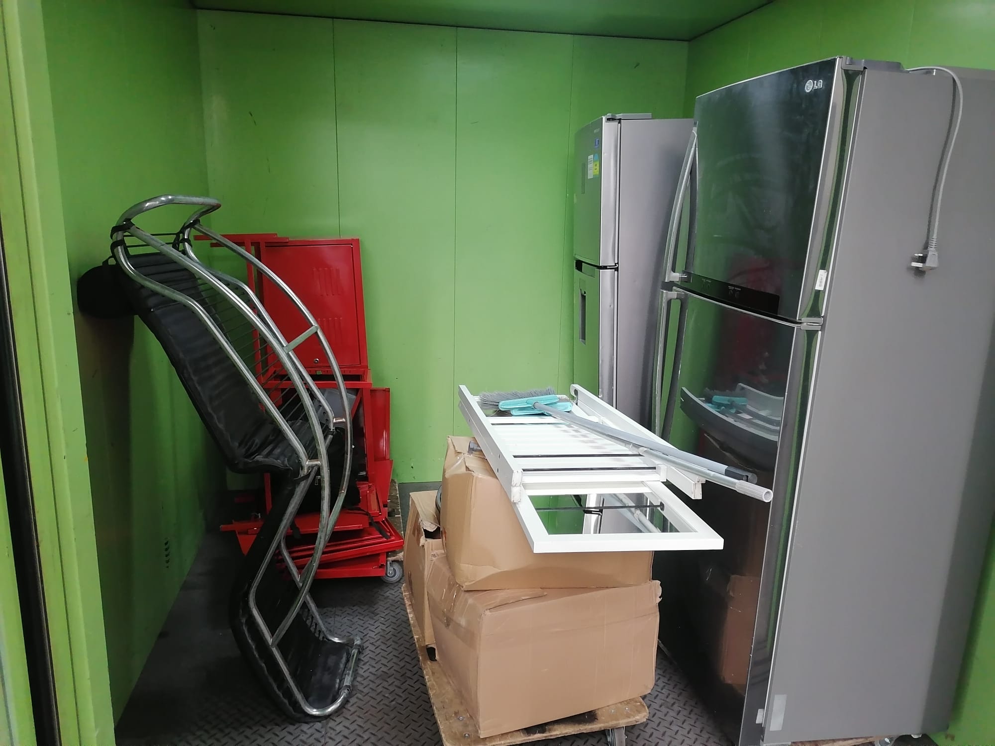 Two large refrigerators, a red cabinet, and a rolling office chair stacked together in a room with green walls.