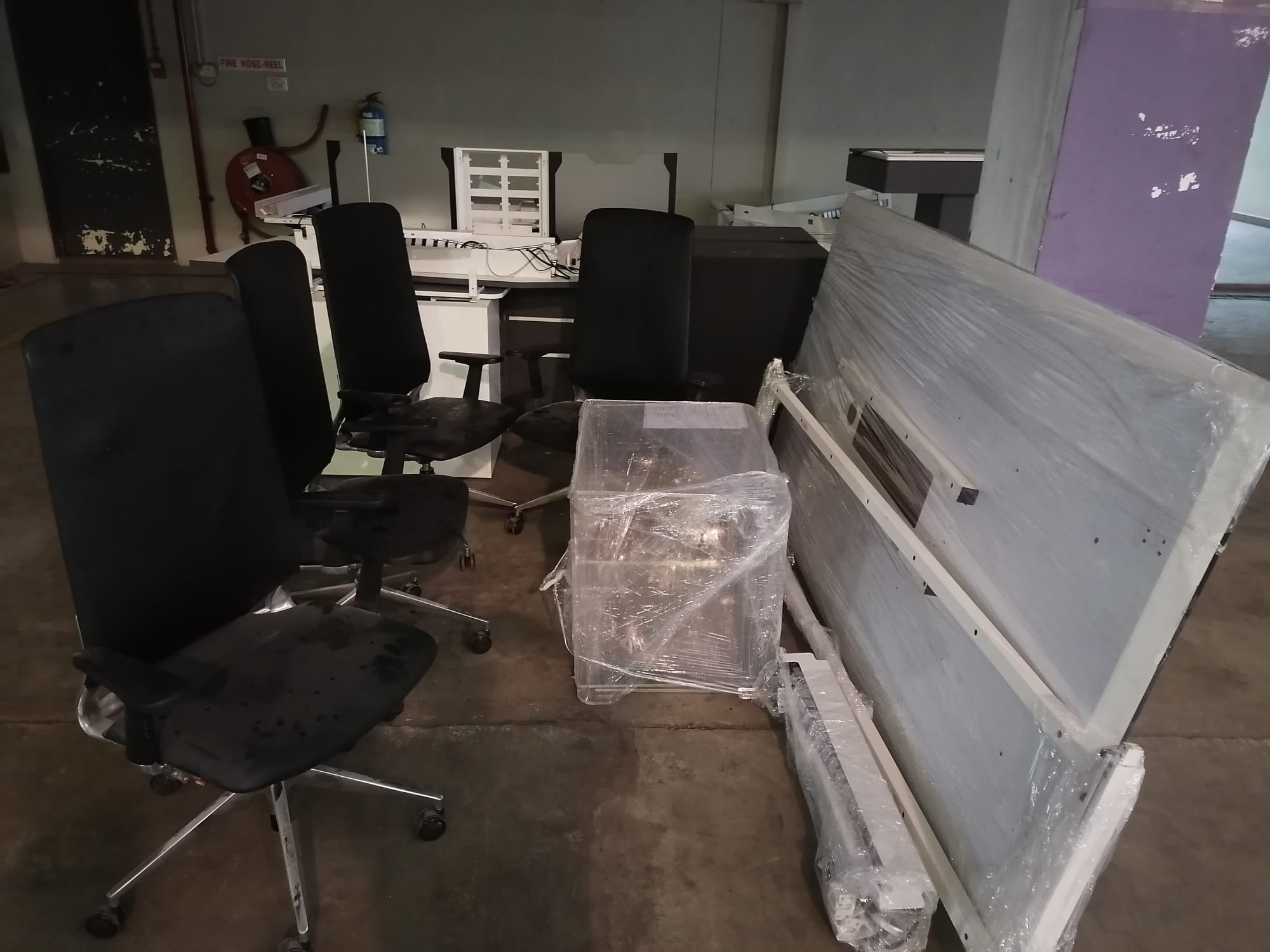Office chairs and large furniture items wrapped in clear plastic, stacked and ready for removal from a commercial workspace.