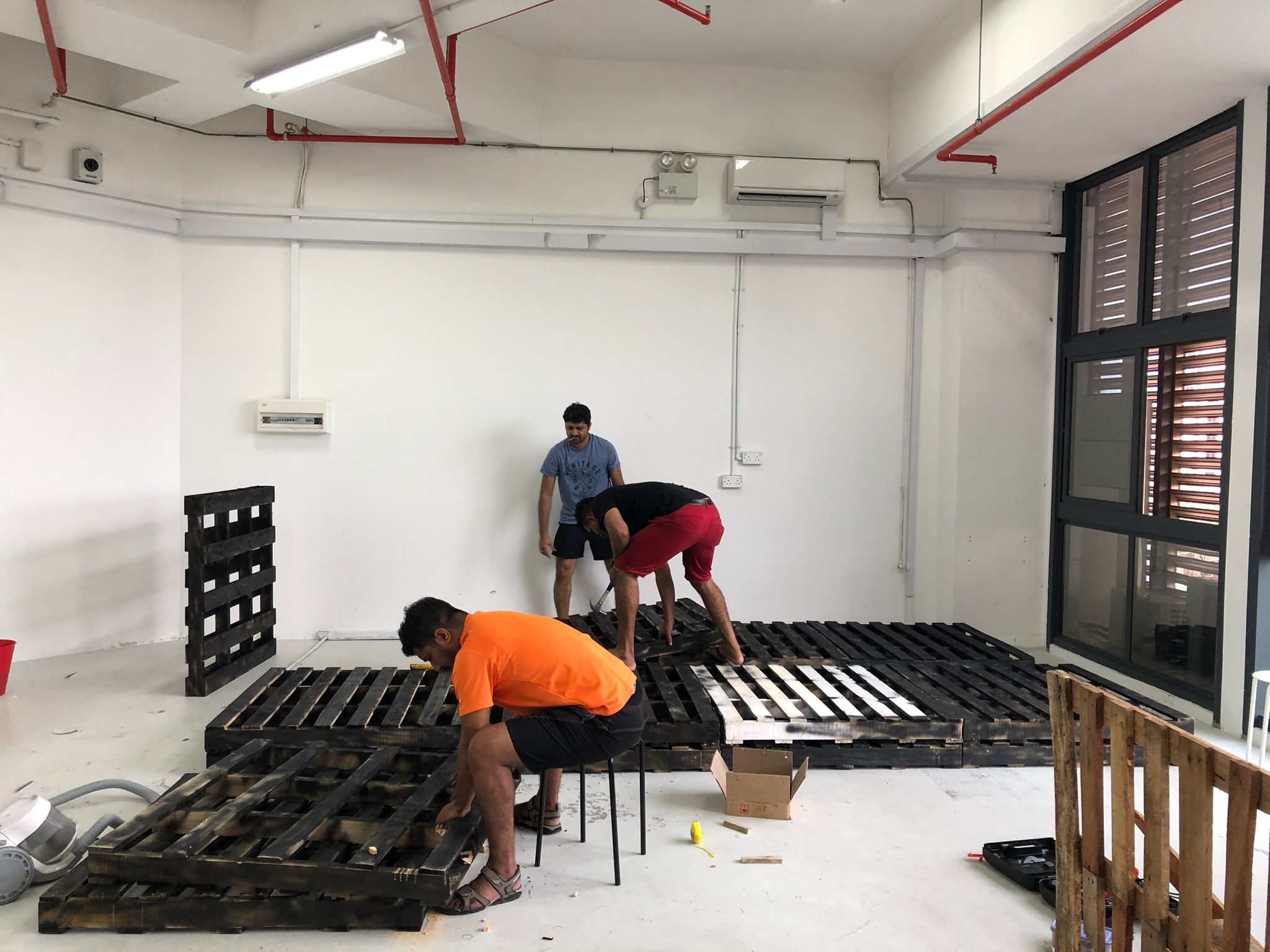 Two workers removing stacked wooden pallets from an empty commercial space.