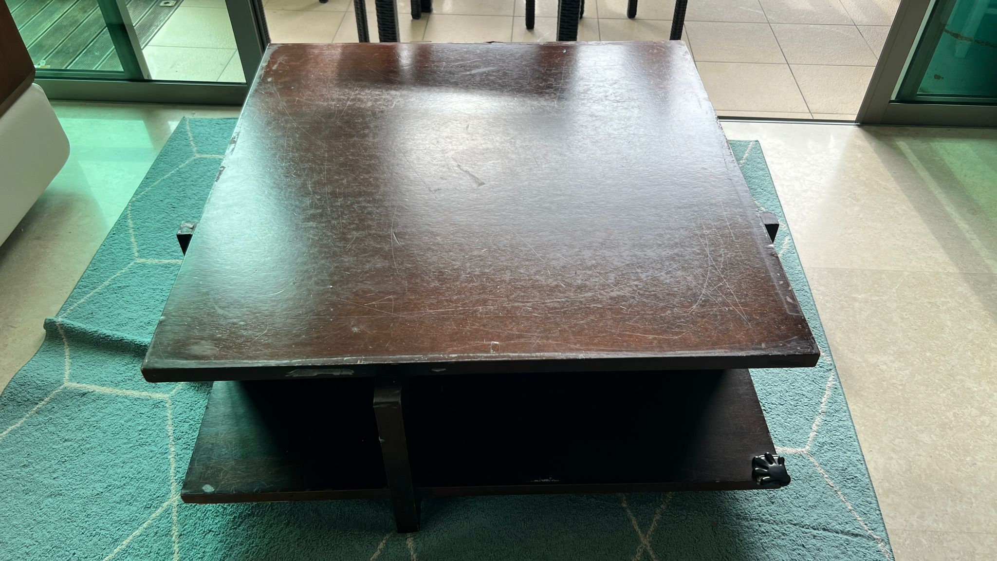 Dark brown wooden coffee table with visible scratches and wear marks, positioned on a teal-coloured rug.